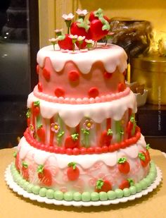 a three tiered cake with strawberries and cherries on the top is sitting on a table