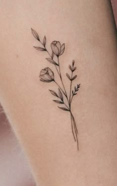 a small flower tattoo on the side of a woman's leg, with leaves