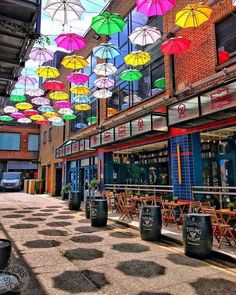 many colorful umbrellas are hanging from the ceiling above an outdoor cafe in a shopping district