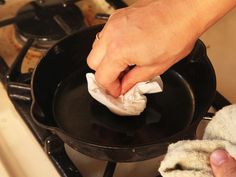 a person holding a cloth over a skillet on top of a stove burner