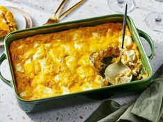 a green casserole dish filled with food next to wine glasses and silverware