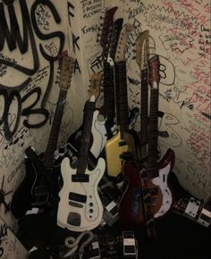 several guitars are lined up against a wall covered in graffiti