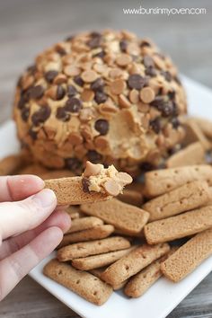 a person holding a cracker in front of a plate of cookies and crackers