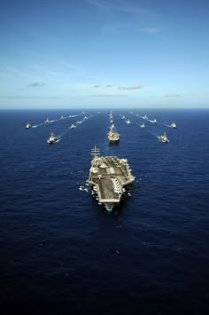 an aircraft carrier in the middle of the ocean surrounded by other ships and smaller ones