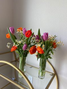 two vases filled with flowers sitting on top of a glass table next to a mirror