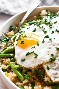 a white bowl filled with rice, asparagus and an egg on top of it