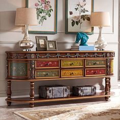 an ornately decorated console table with two lamps and pictures on the wall behind it