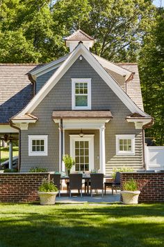 a small gray house with white trim and windows on the front, sitting in grass