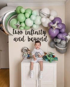 a young boy sitting on top of a white cabinet in front of balloons and decorations