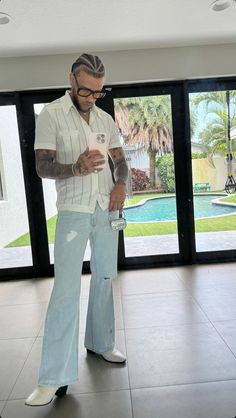 a man in white shirt and blue jeans looking at cell phone while standing on tiled floor