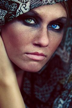 a woman with blue eyes wearing a bandana and looking at the camera while holding her hand on her head