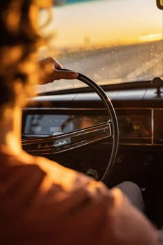 a woman driving a car with the sun setting in the background and her hand on the steering wheel