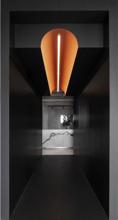 an orange light hanging from the ceiling in a room with black walls and flooring