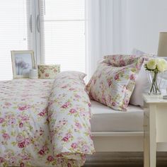 a white bed with pink and yellow flowers on it next to a window in a bedroom