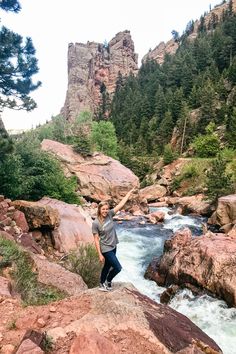 a woman standing on top of a large rock next to a river with rocks in it