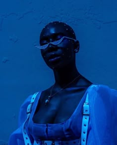 a woman with dark skin wearing blue and silver accessories, standing in front of a blue wall