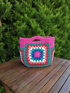 a crocheted bag sitting on top of a wooden table next to some bushes