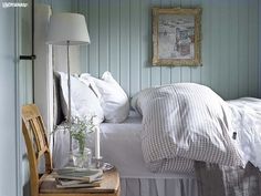 a white bed sitting next to a wooden table with a lamp on top of it