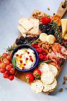 an assortment of cheeses, crackers, fruit and nuts on a cutting board