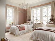 two beds in a bedroom with white and pink bedding, chandelier and windows