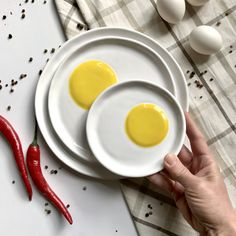 two eggs are sitting on white plates next to red chili peppers and an egg shell