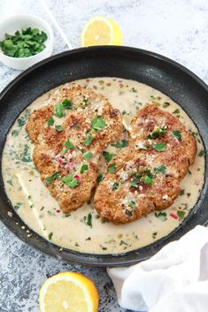 two chicken patties are in a skillet with cream sauce and garnished with parsley