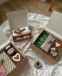 two open boxes filled with gifts on top of a white sheet covered table next to a candle