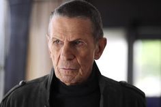 an older man looking at the camera while wearing a black shirt and leather jacket with his hands on his hips