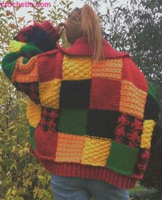 a woman wearing a multicolored knitted jacket and hat looking at the trees