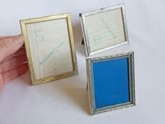 two small silver and blue frames sitting on top of a white table next to each other