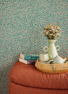 there is a vase with flowers and two cups on top of a stool next to books