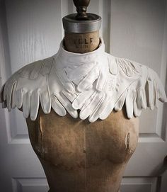 a mannequin with white leather wings on it's neck and collar, standing in front of a door