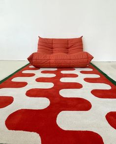 a large red and white rug on the floor in front of a couch with pillows