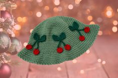 a crocheted green hat with cherries hanging from it's brim