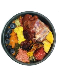 a bowl filled with assorted fruits and meats on top of a white table