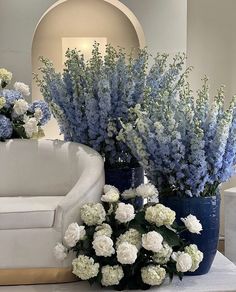 two blue vases with white flowers on a table in front of a couch and mirror