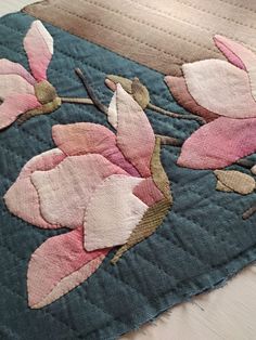 an embroidered piece of fabric with pink flowers and leaves on blue background, closeup