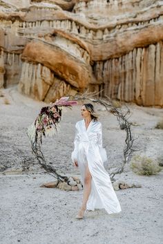 a woman in a white dress is walking through the desert with a wreath around her