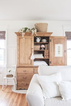 a living room with white furniture and flowers on top of the hutch in the corner