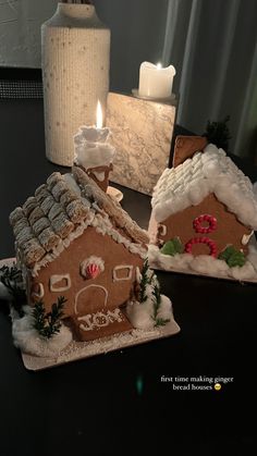 two gingerbread houses are sitting on a table next to a lit candle and some candles