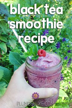 a hand holding a mason jar filled with black tea smoothie and raspberries