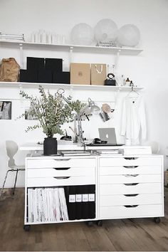 a white desk topped with a laptop computer next to a shelf filled with books and magazines