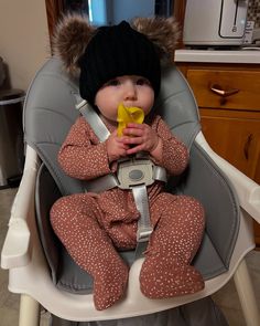 a baby sitting in a high chair with a pacifier in its mouth and wearing a hat