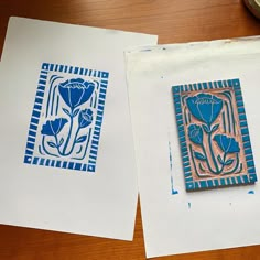 two pieces of paper with blue flowers on them sitting on a table next to each other