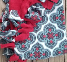 a red and grey blanket with blue flowers on it sitting next to a wooden fence