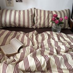 a bed with red and white striped comforter next to a vase filled with pink roses