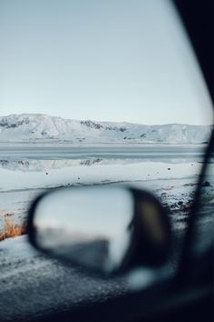 the side view mirror of a car with mountains in the background and snow on the ground