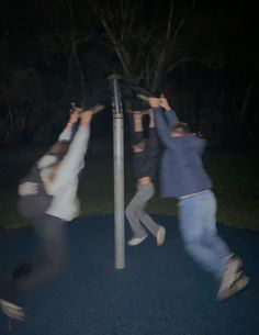 three people jumping up in the air on a street pole at night with one person upside down