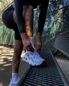 a woman tying up her shoes on the side of a metal bench in front of some trees