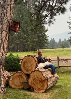 a woman sitting on top of a pile of logs next to a tree